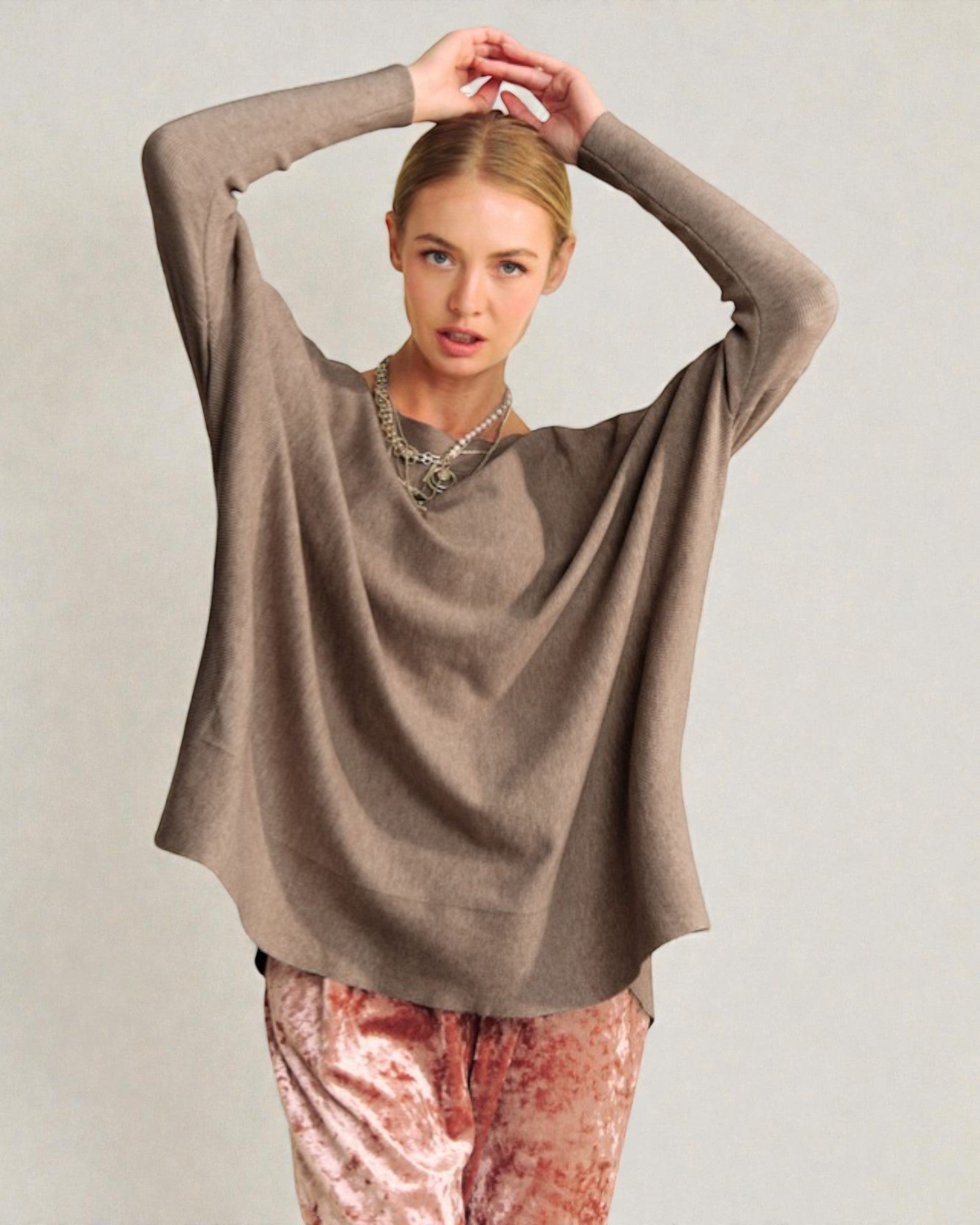 Woman wearing a brown sweater and pink pants against a plain background