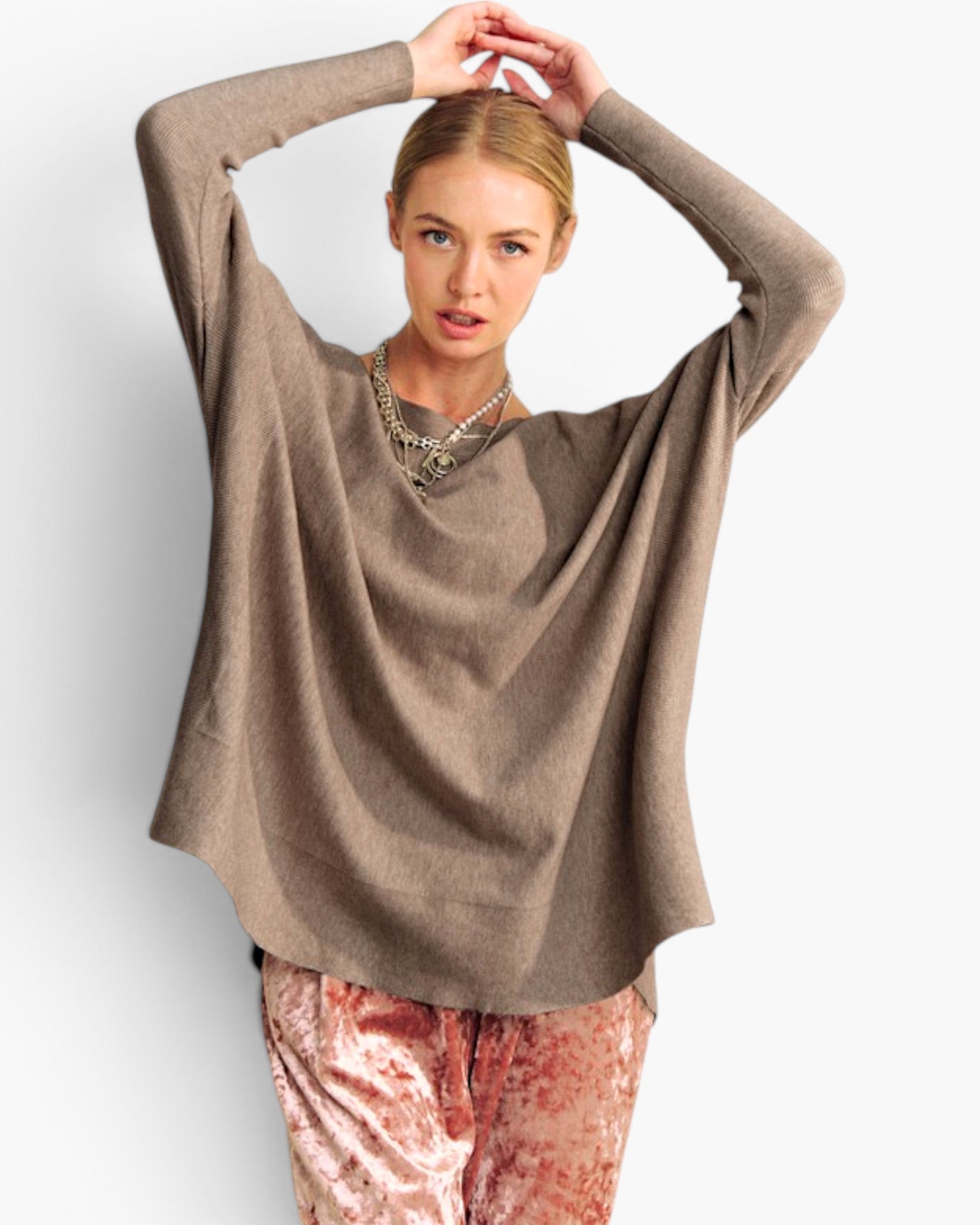 A woman modeling a loose, draped long-sleeve knit top in taupe brown, paired with pinkish-red patterned pants, against a plain light gray studio background.
