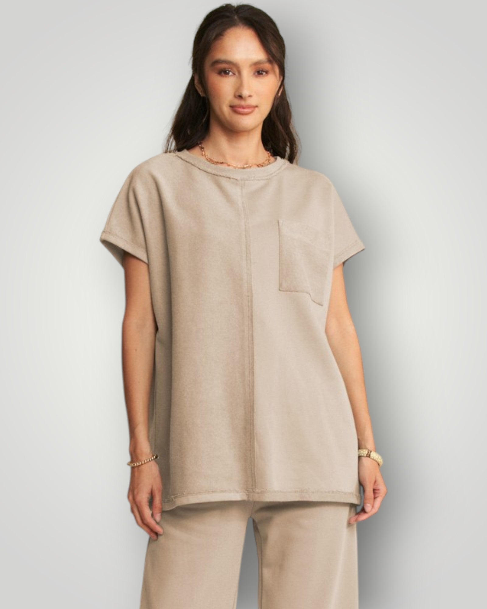 Woman wearing a beige tunic and pants on a plain background