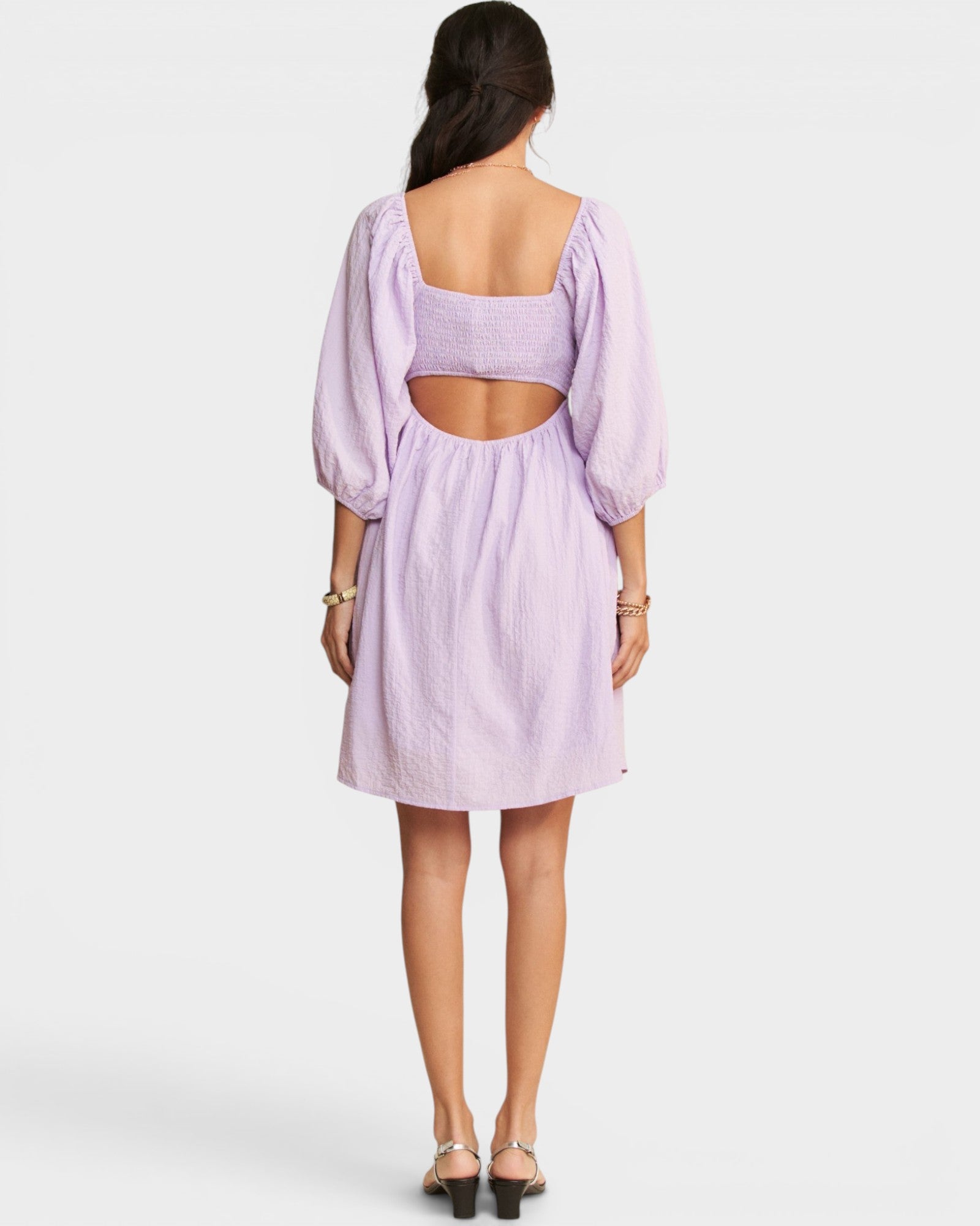 Woman wearing a light purple dress with cut-out back on a white background