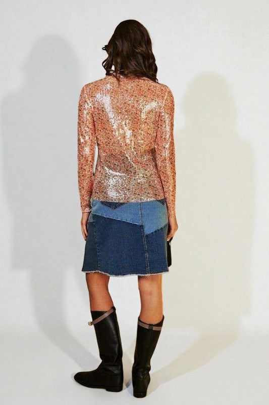 Person wearing a sequined top and denim skirt with black boots on a white background
