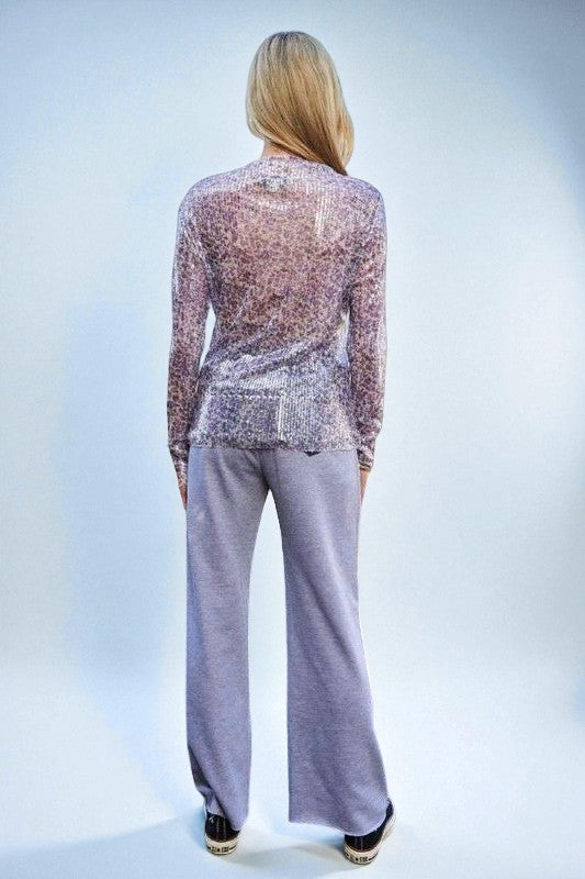 Person wearing a sheer sequin top and gray pants on a light blue background