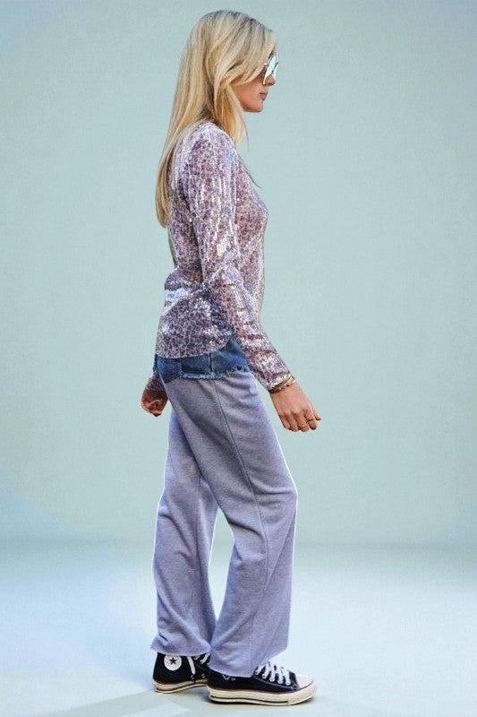 Woman wearing a patterned top and light purple pants with black sneakers on a light blue background