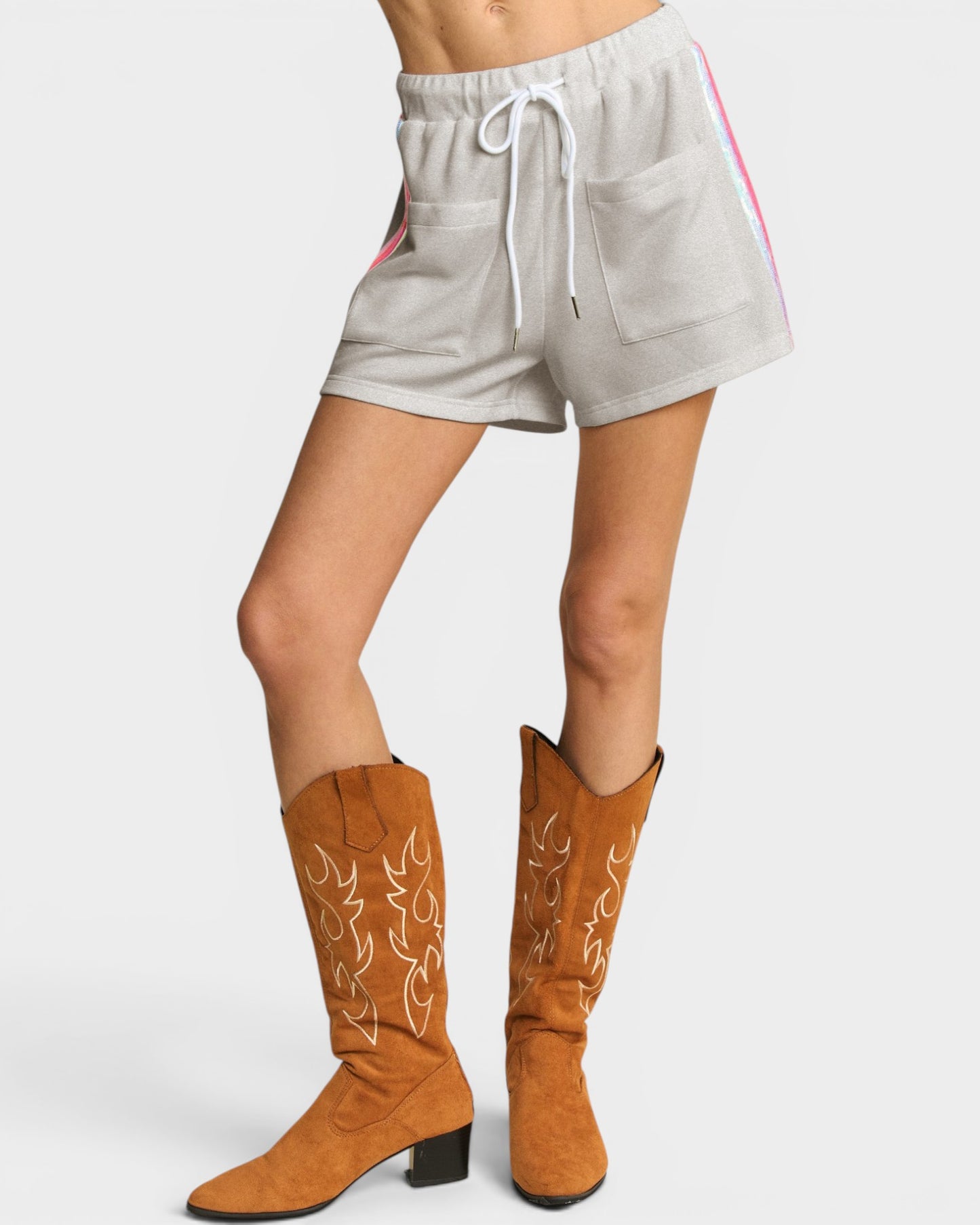 Person wearing tan cowboy boots and gray shorts on a white background