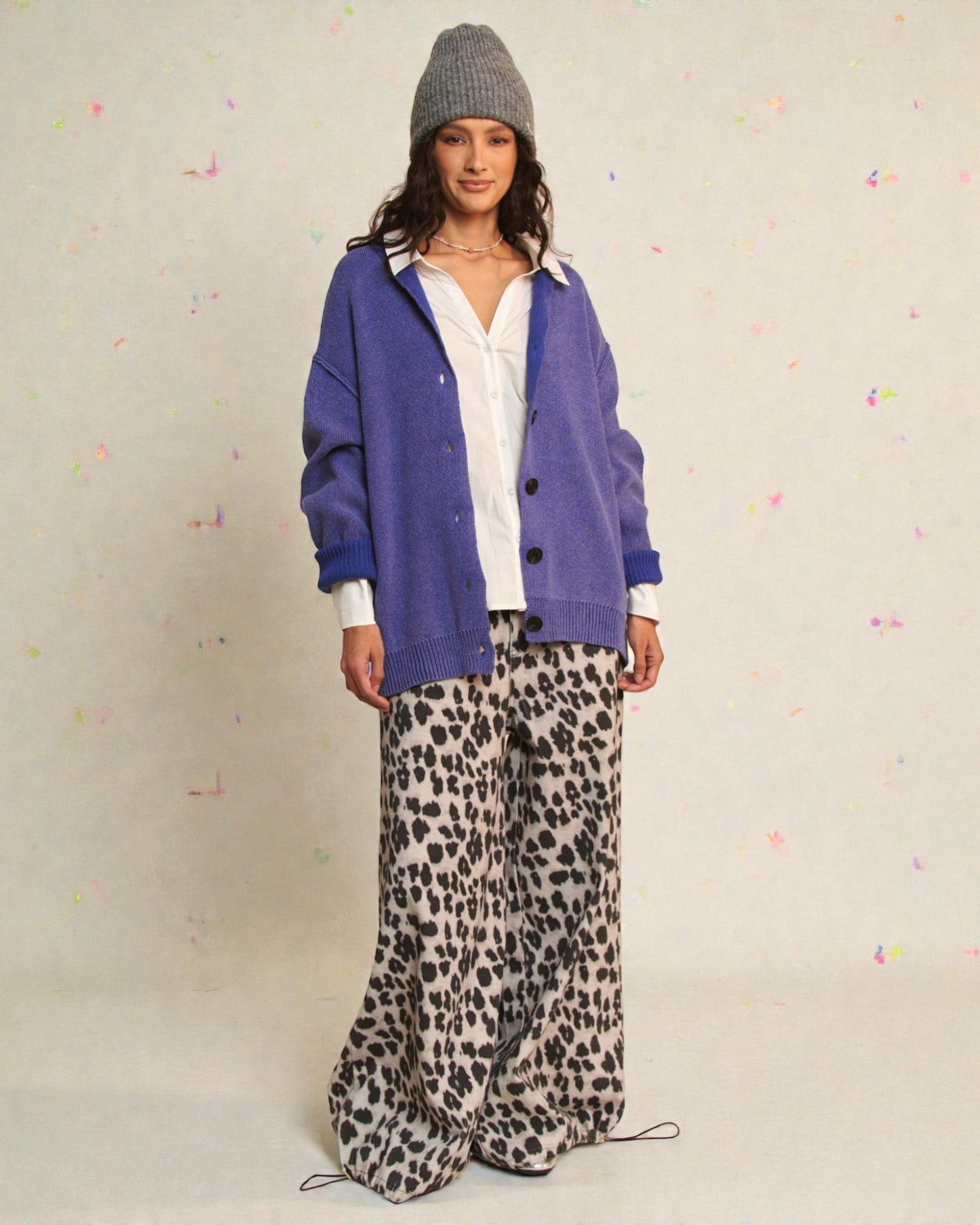 Woman wearing a blue cardigan, white shirt, and leopard print pants on a light background