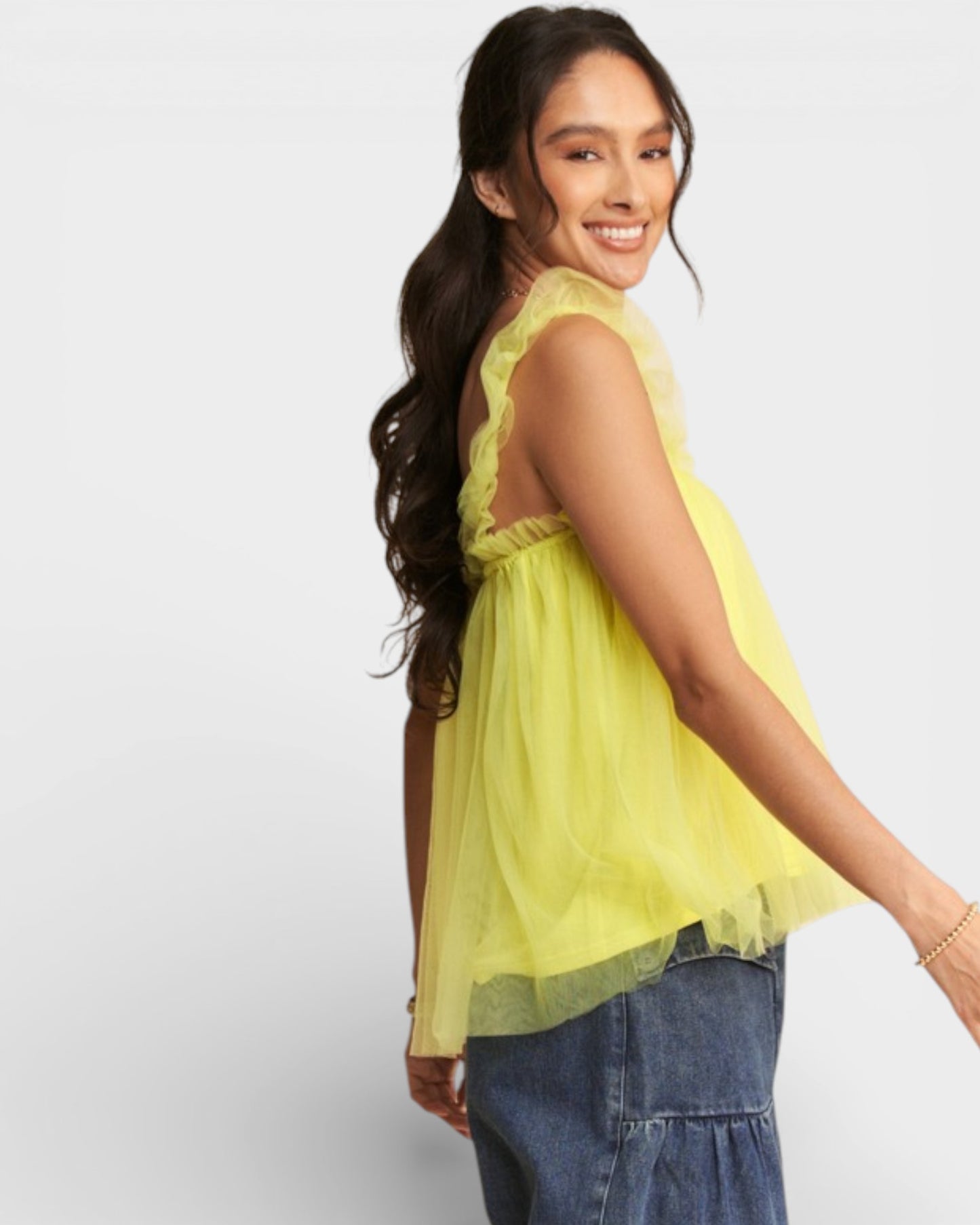 Woman wearing a yellow sheer top and blue jeans on a white background