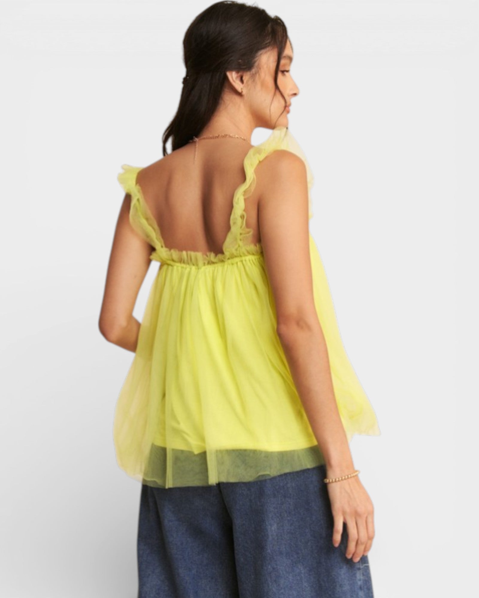 Woman wearing a yellow sheer top with blue pants on a white background