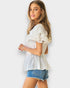 Woman wearing a white blouse with ruffled sleeves and denim shorts against a white background