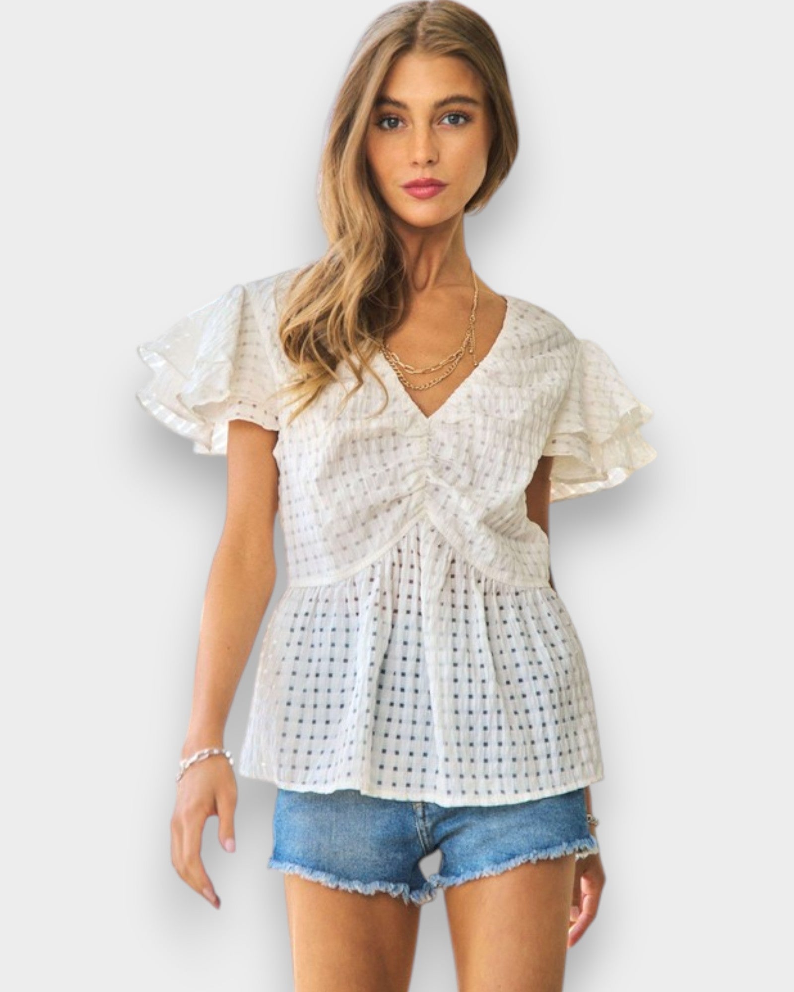 Woman wearing a white lace top and denim shorts on a plain background