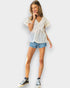 Woman wearing a white lace top and denim shorts against a white background