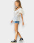 Woman wearing a white blouse, denim shorts, and black sneakers on a plain background