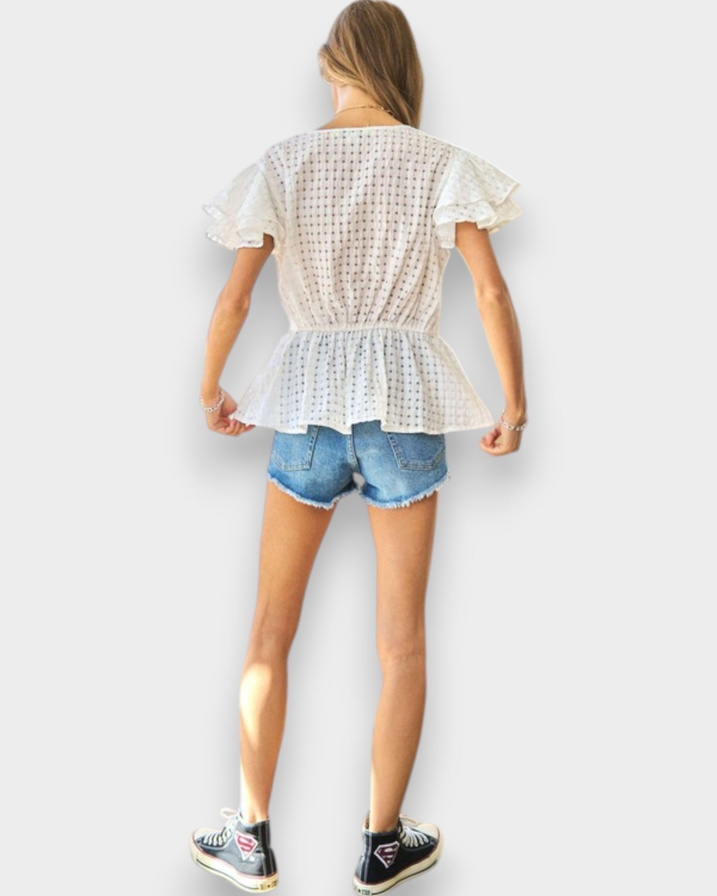 Person wearing a white ruffled top and denim shorts on a plain background