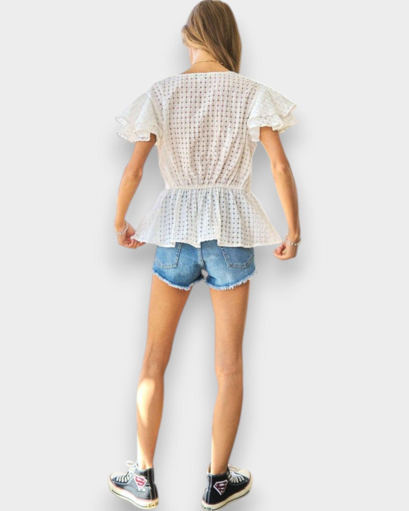 Person wearing a white ruffled top and denim shorts on a plain background