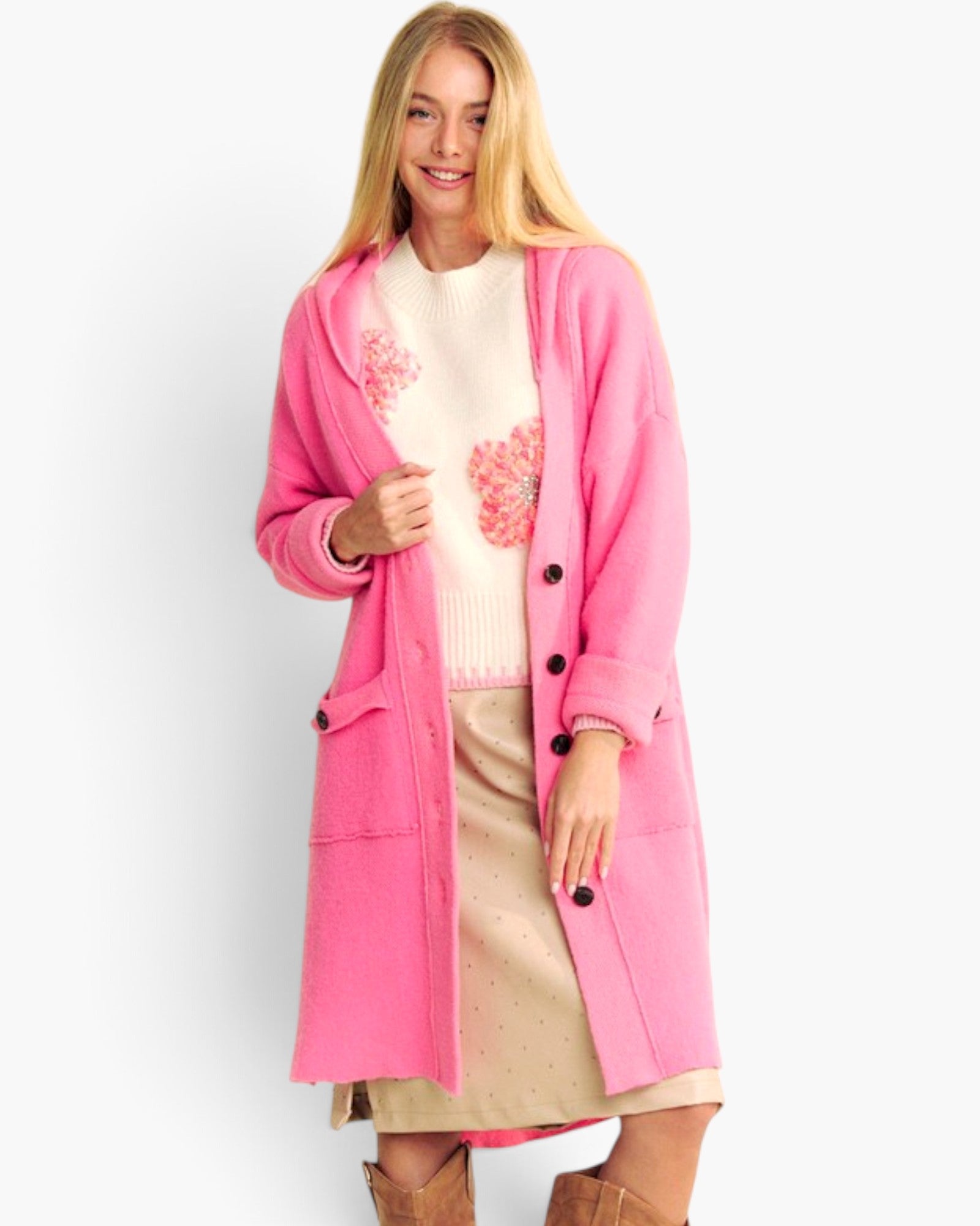 A woman modeling a bright pink long cardigan over a cream sweater with pink floral embroidery and a beige skirt, against a plain white studio background.