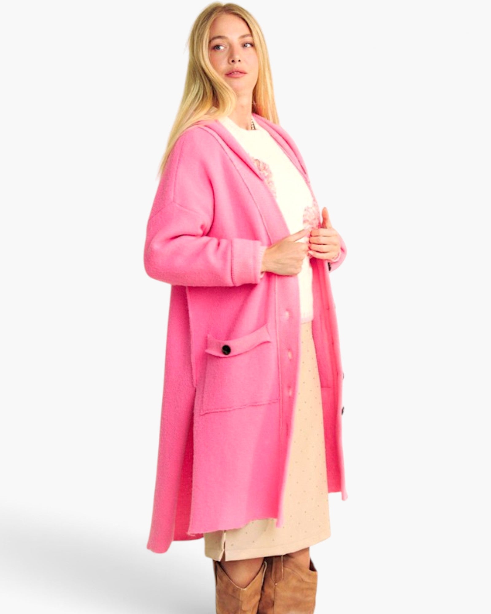 A woman modeling a bright pink open-front cardigan over a cream dress, standing against a plain light gray studio background.