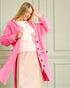 Woman wearing a pink coat over a light pink outfit with a floral pattern against a light green wall.