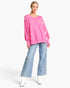 A model wearing a bright pink crewneck sweater with white stripe accents on the sleeves, paired with light blue wide-leg jeans featuring star embroidery and white pointed boots, set against a plain white studio background.