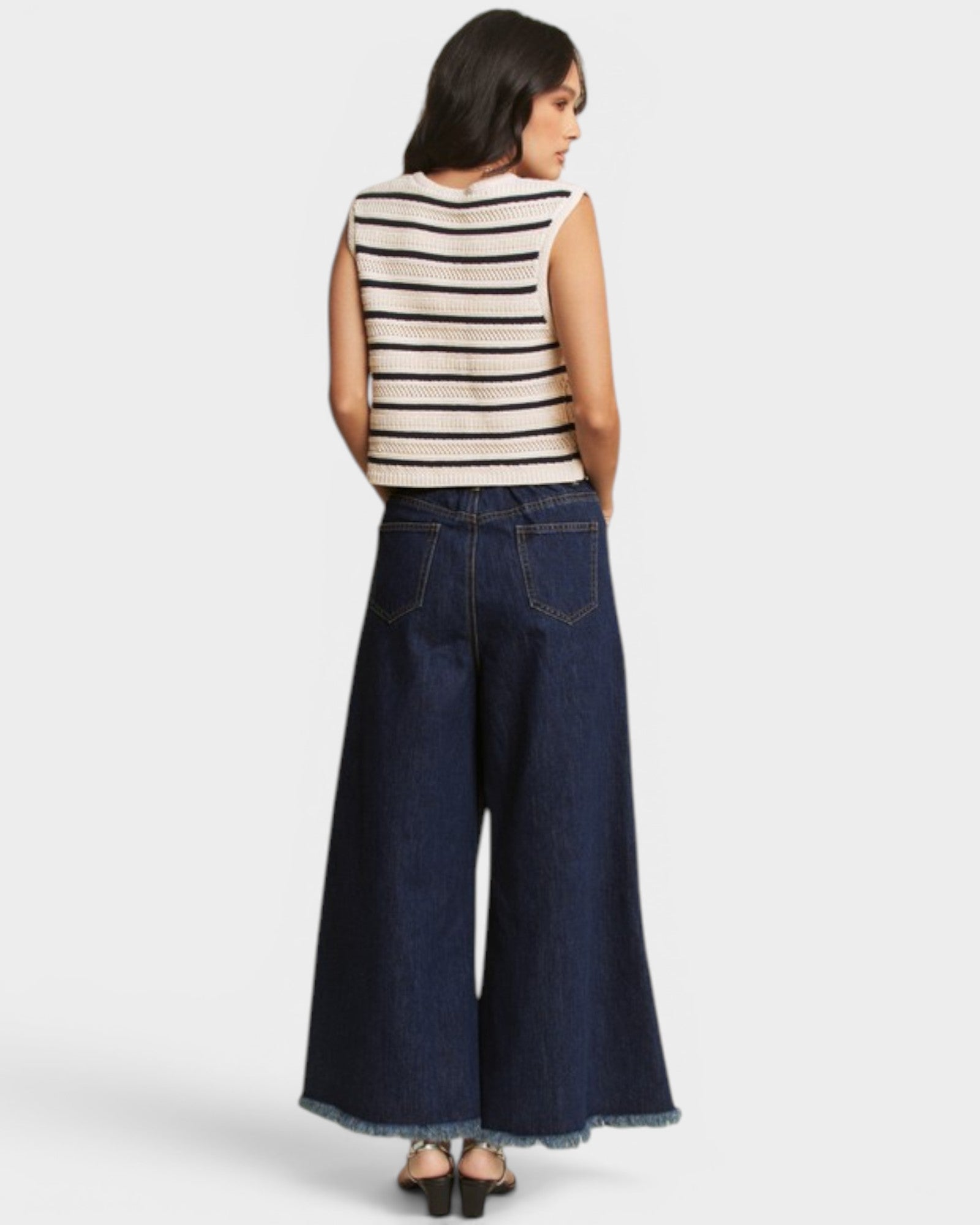 Woman wearing a striped sleeveless top and wide-leg jeans on a white background