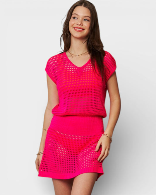 Woman wearing a bright pink crochet top and skirt on a white background