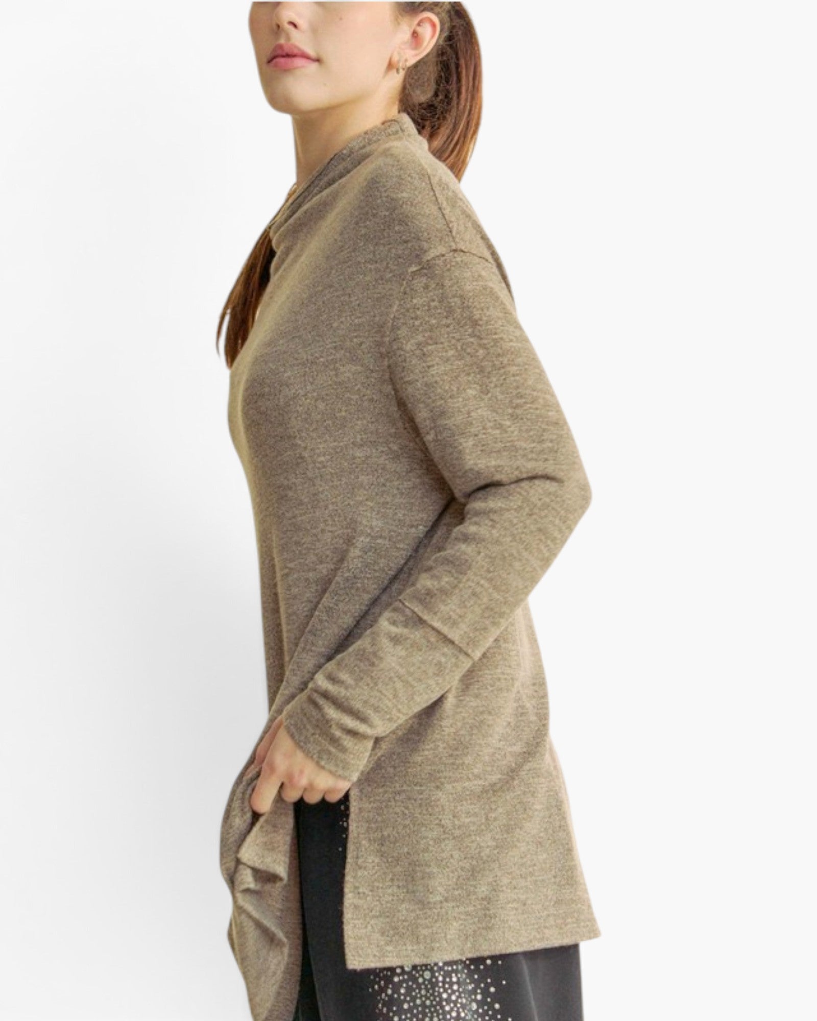A woman shown in side profile wearing a long-sleeve, heathered taupe knit tunic sweater with a high collar and side slit, paired with black pants against a plain white studio background.