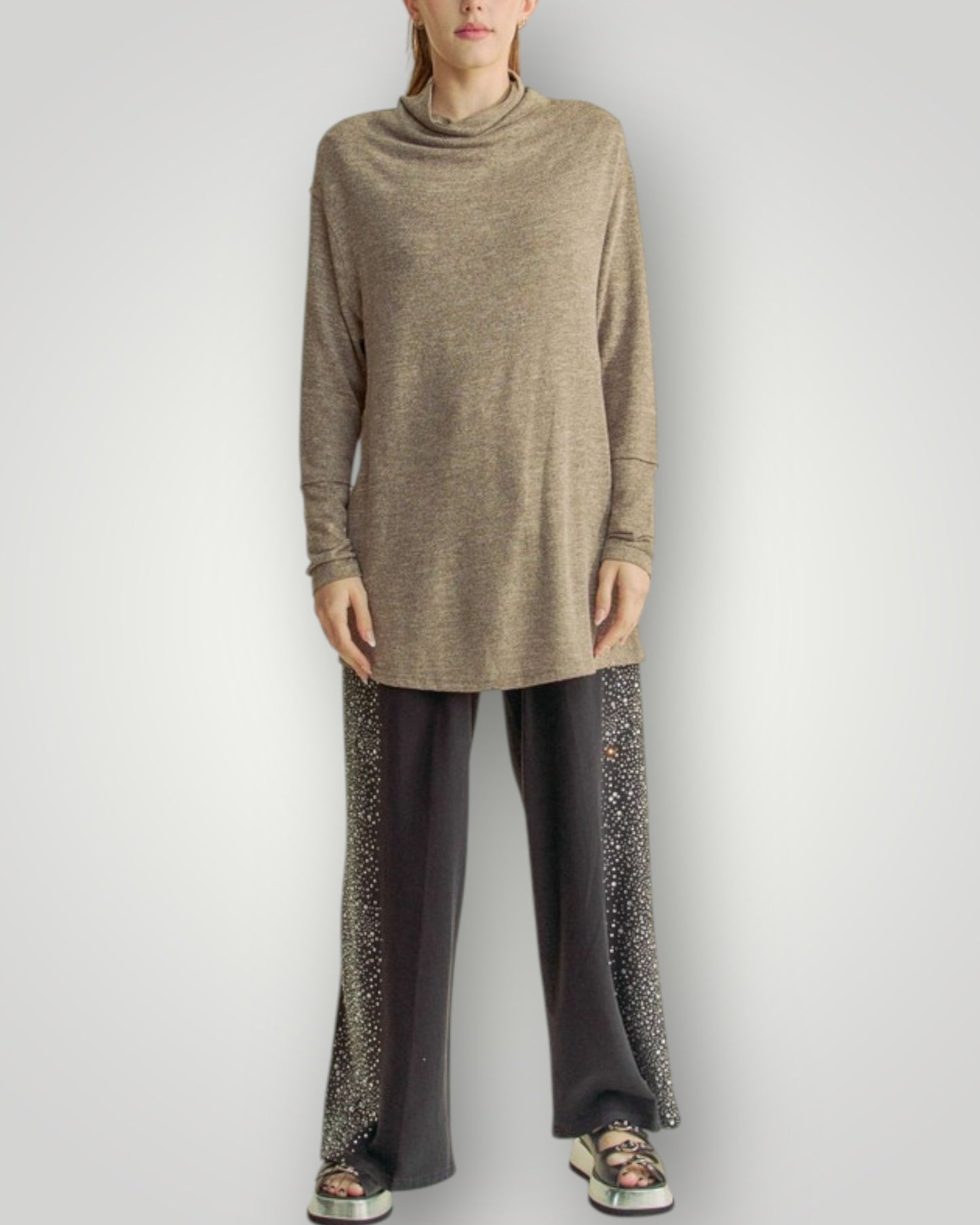 Person wearing a long beige sweater and dark pants on a white background