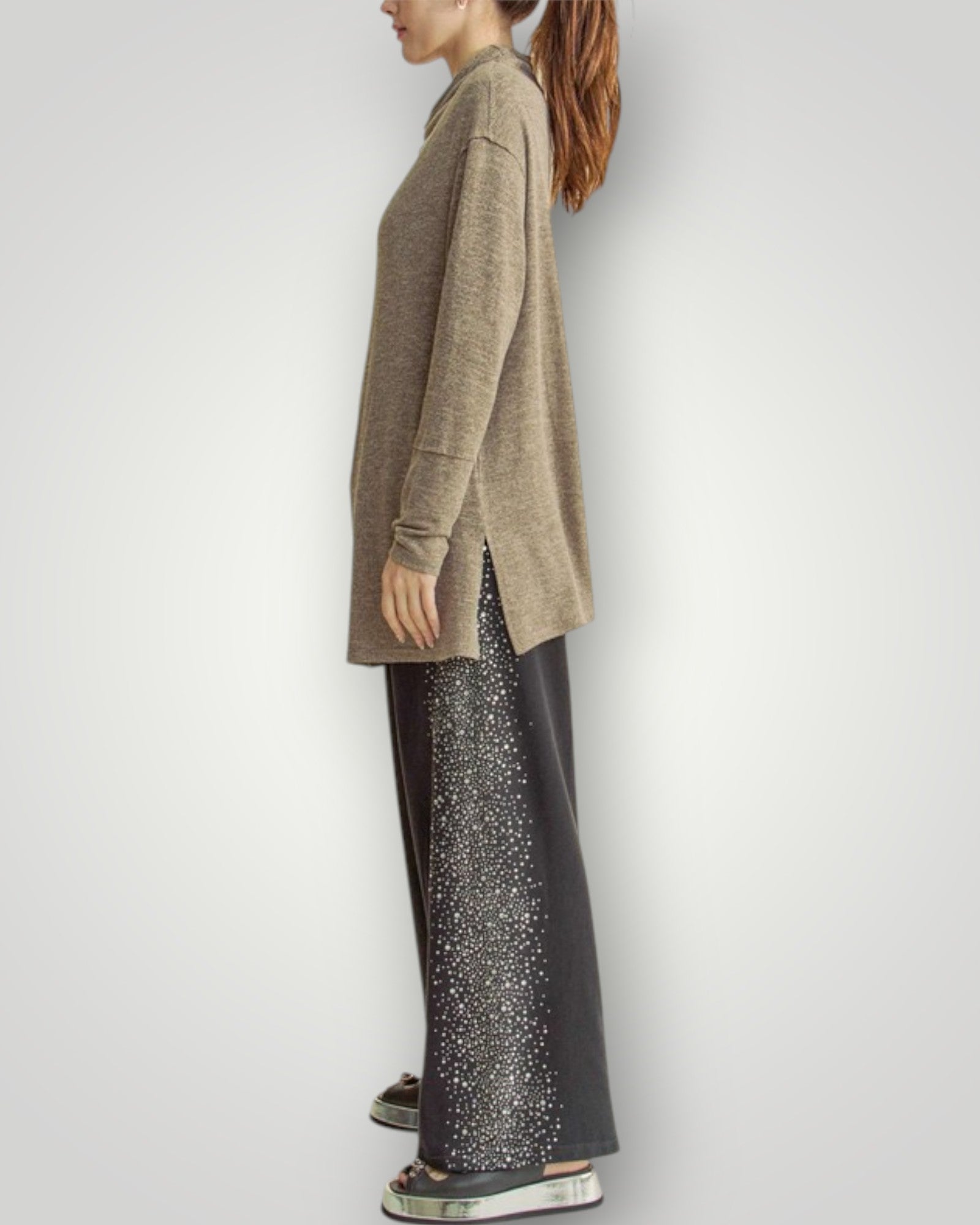 Person wearing a beige sweater and black pants with white patterns on a white background