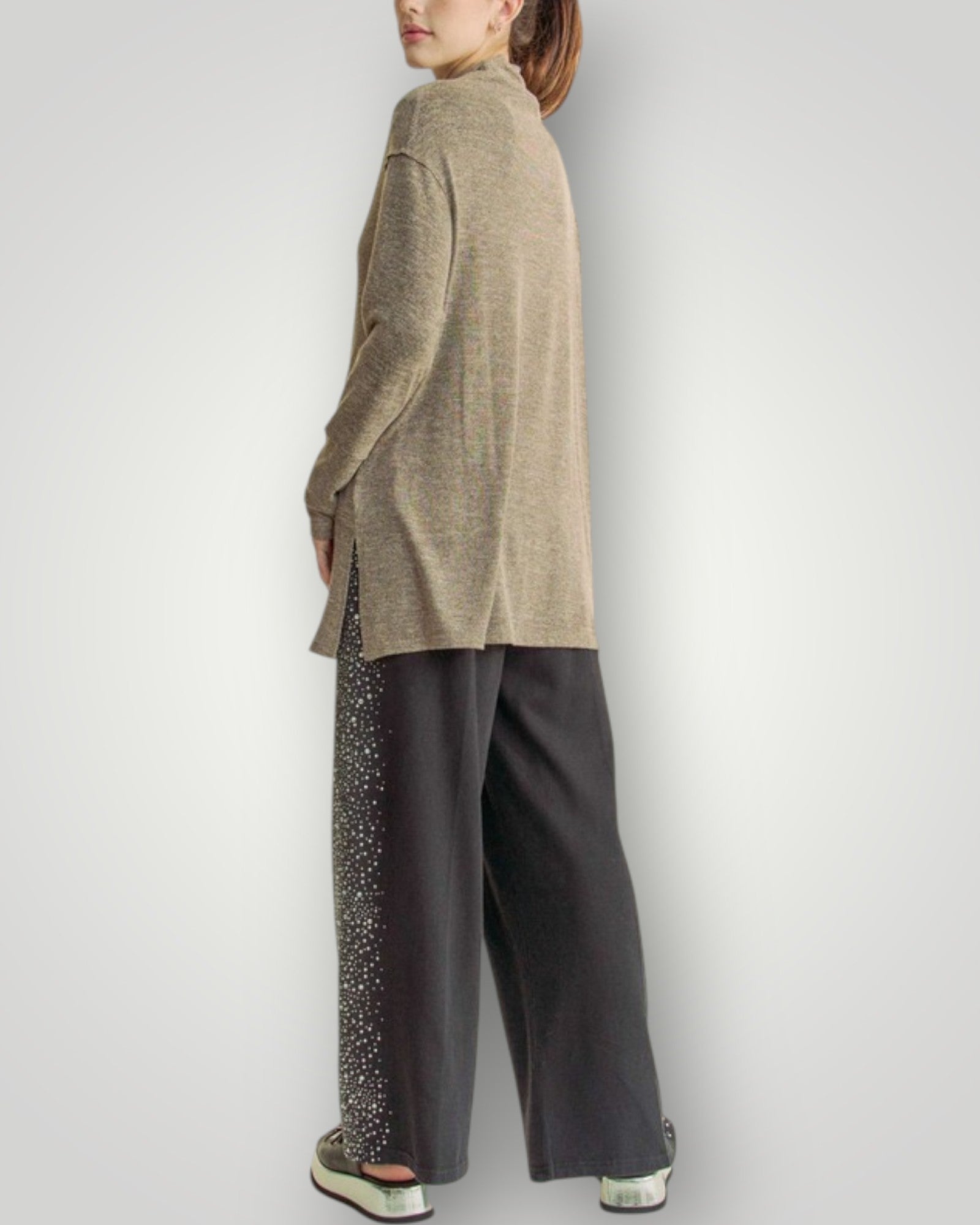 Person wearing a beige sweater and dark pants on a white background