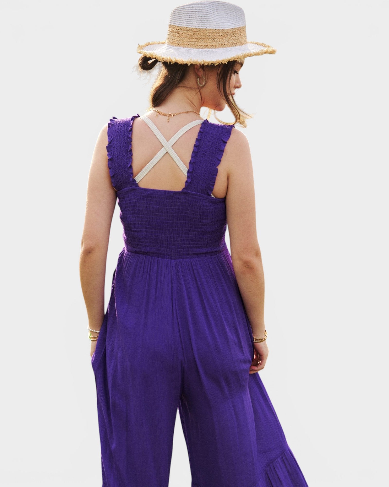 Woman wearing a purple jumpsuit with a white hat on a plain background