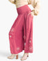 A model wearing high-waisted, wide-leg pink pants with 3D floral embroidery and sequin details, paired with a beige cropped top and beige heels against a light gray background.