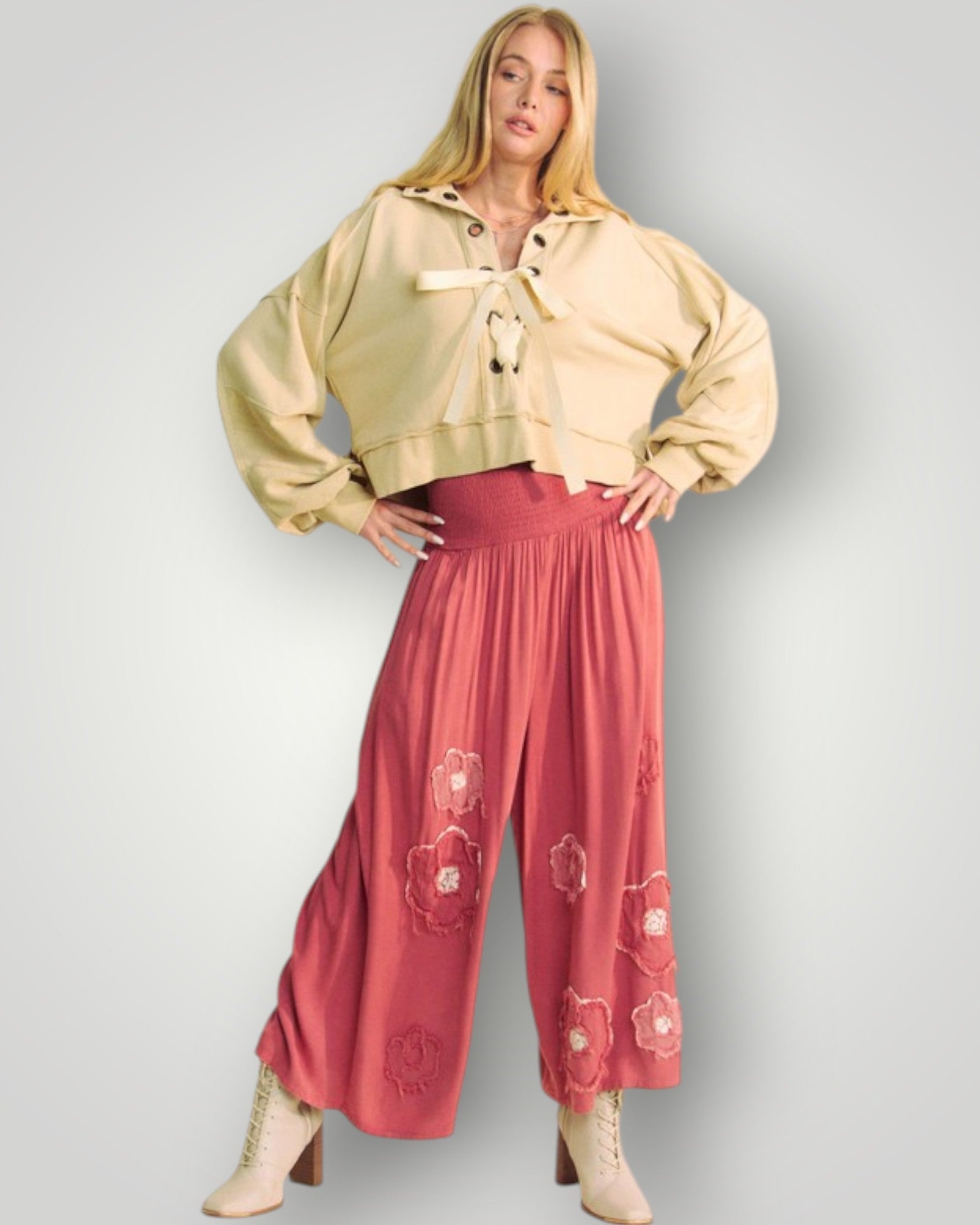 Woman wearing a beige jacket and pink pants with floral patterns on a gray background