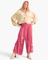 A model wearing a beige cropped tie-front jacket and pink wide-leg pants with floral embroidery, posed against a light gray studio background.
