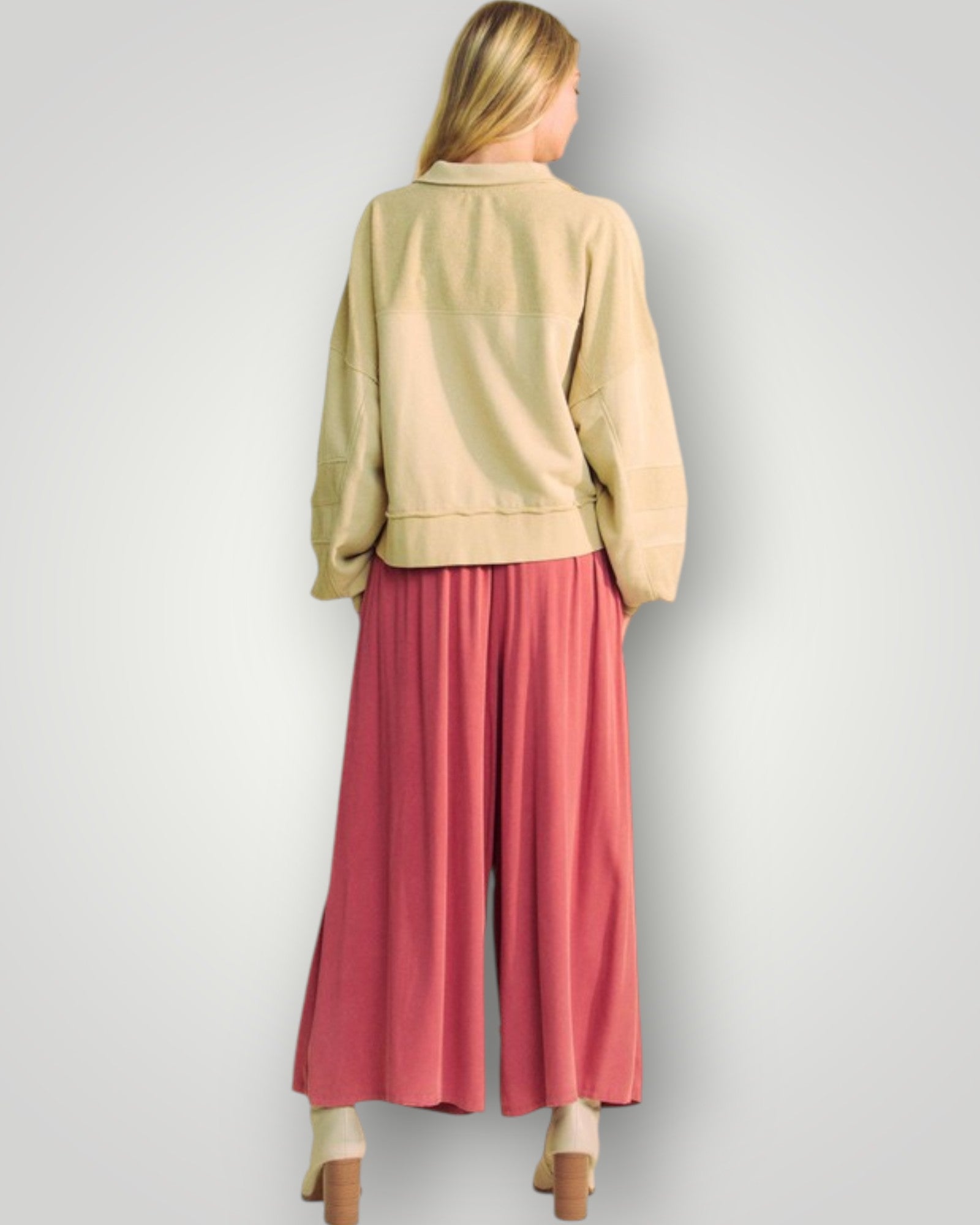 Woman wearing a beige jacket and pink pants on a plain background