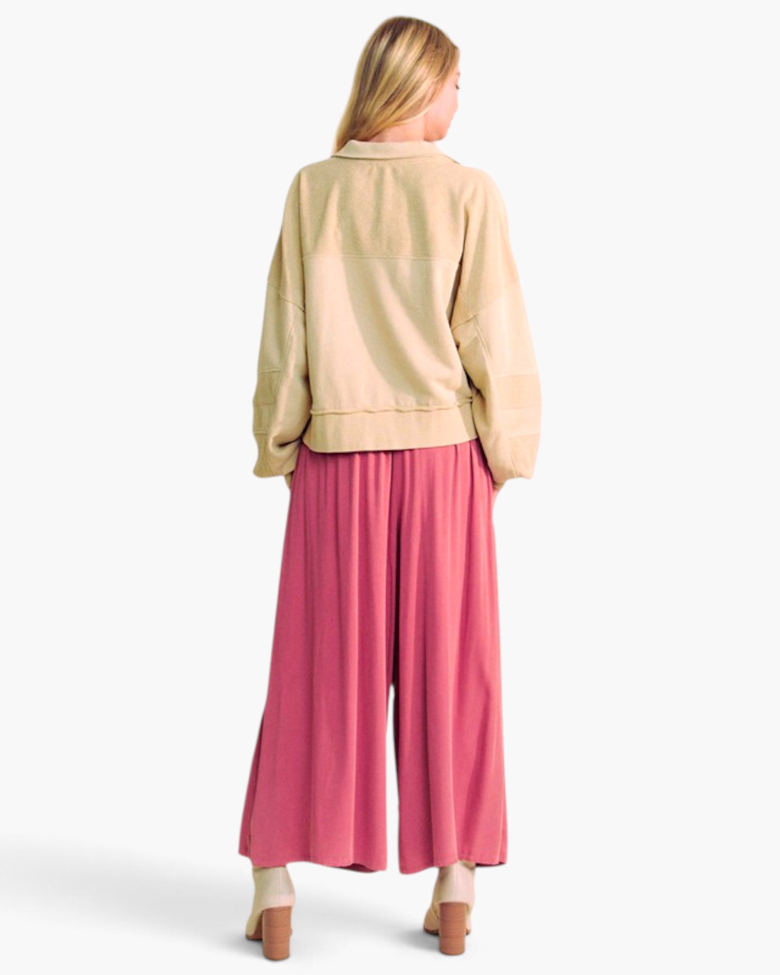 A woman shown from the back wearing a beige cropped jacket and bright pink wide-leg pants, photographed against a clean white studio background.
