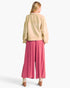 A woman shown from the back wearing a beige cropped jacket and bright pink wide-leg pants, photographed against a clean white studio background.