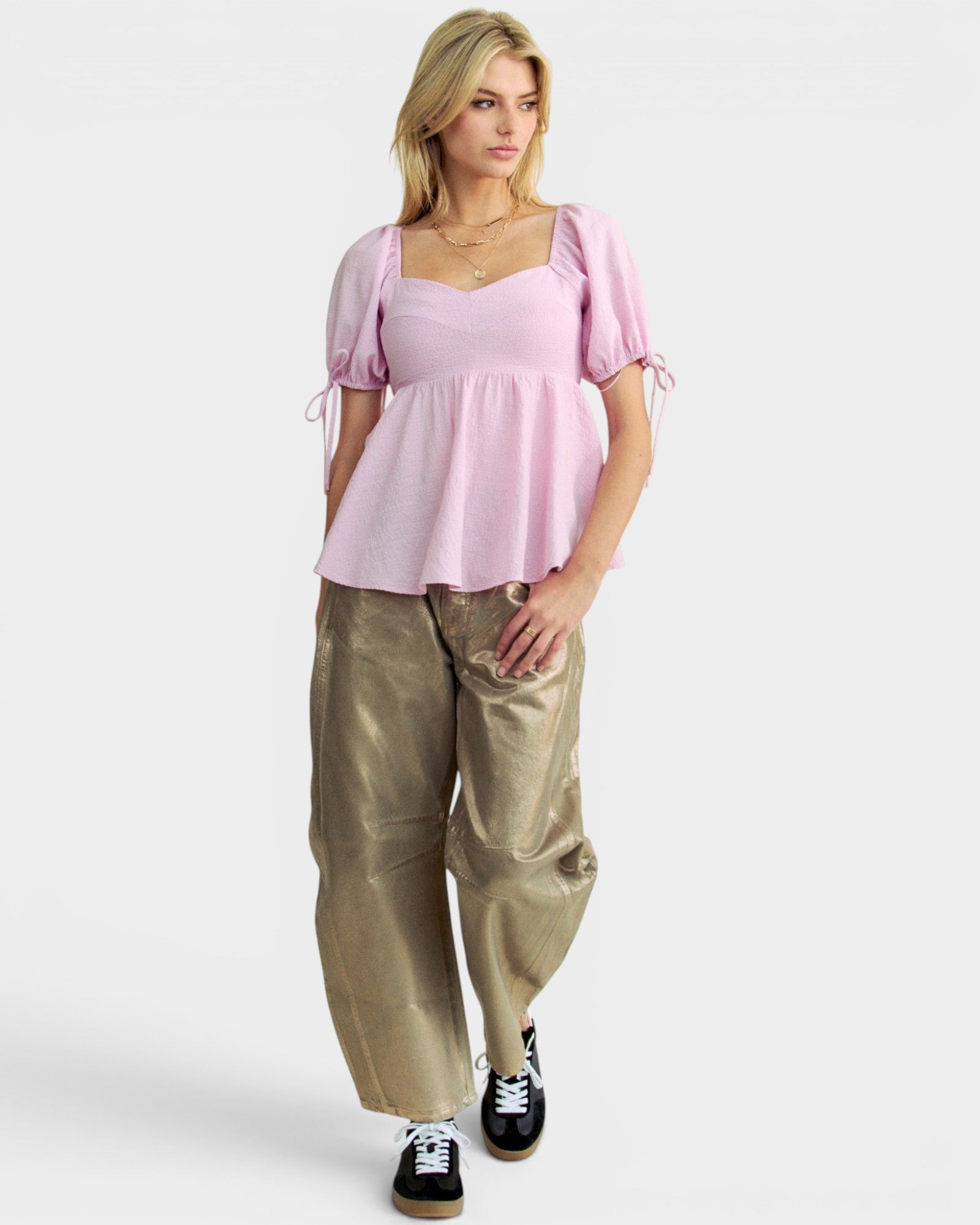 Woman wearing a pink top and gold pants on a white background