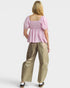 Woman wearing a pink top and beige pants on a white background