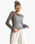 A woman modeling a sheer black mesh long-sleeve top over a silver patterned camisole, paired with off-white drawstring pants, against a plain white background.