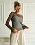 Woman wearing a layered outfit with a patterned top and plain pants in a white room.