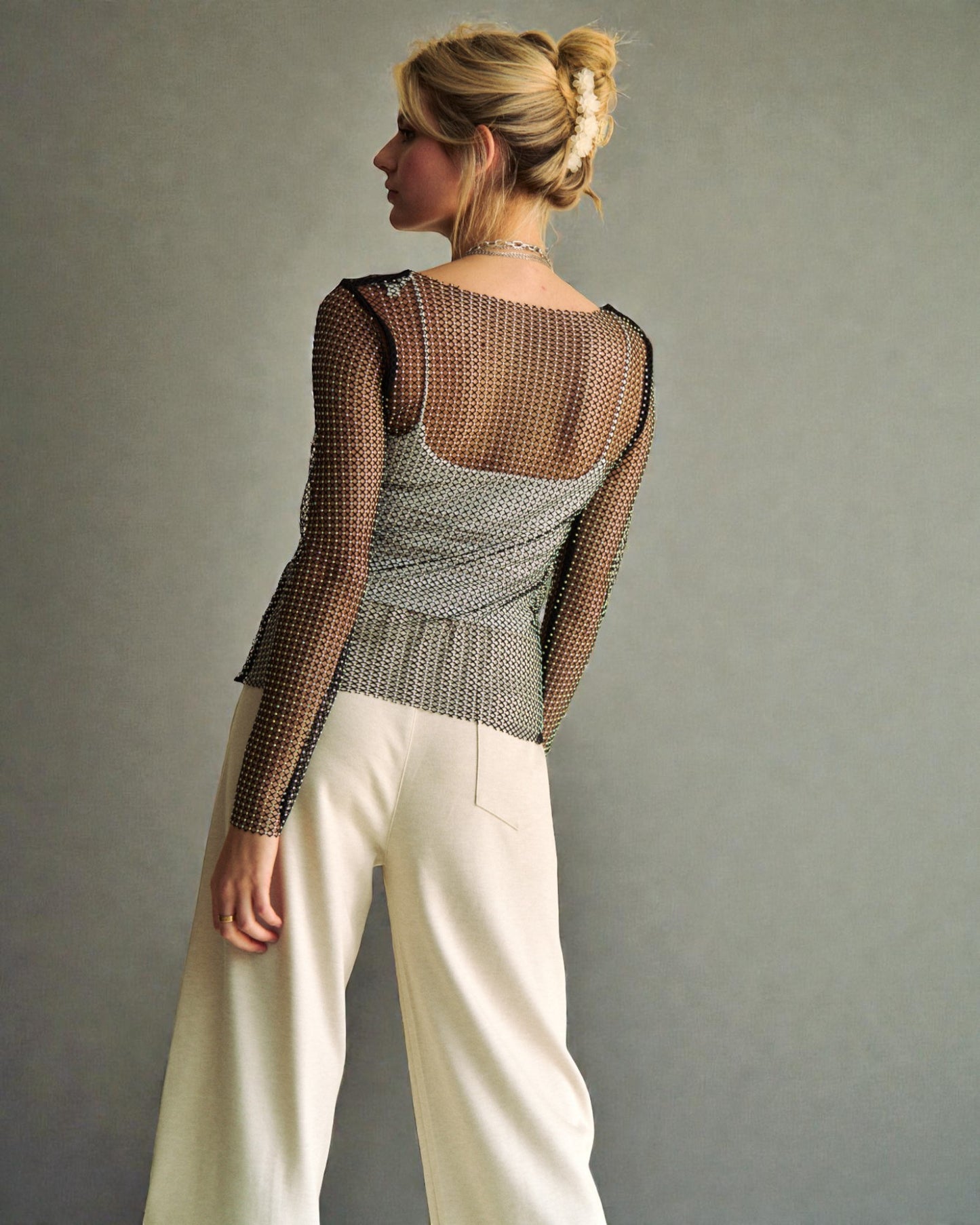 Woman wearing a mesh top and white pants against a plain background