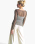 A woman shown from the back wearing a sheer black mesh long-sleeve top over a gray patterned camisole, paired with white wide-leg pants, against a plain white background.