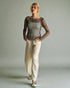 Woman wearing a sheer top and beige pants against a plain background