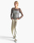 A woman modeling a sheer black mesh long-sleeve top with a silver and black checkered bodice, paired with cream-colored wide-leg pants and metallic sandals, against a plain white background.