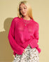 Woman wearing a bright pink sweater with a star design against a beige background