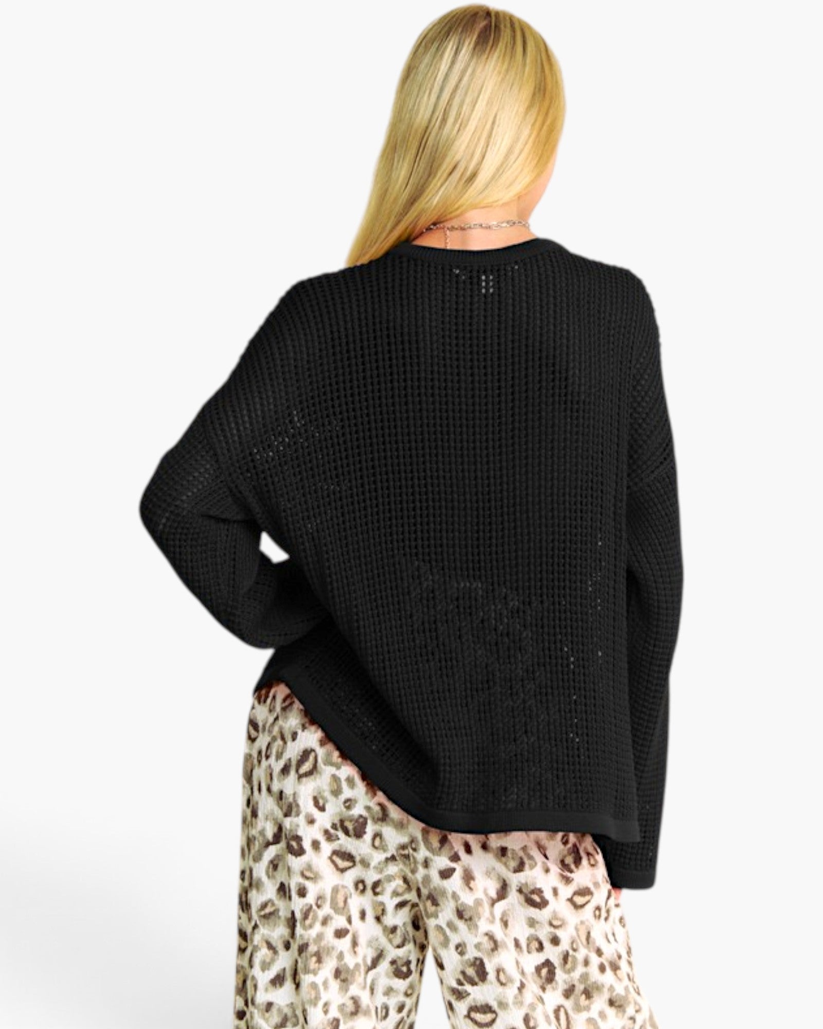 A woman shown from the back wearing a black waffle-knit sweater and leopard-print pants against a plain white background.