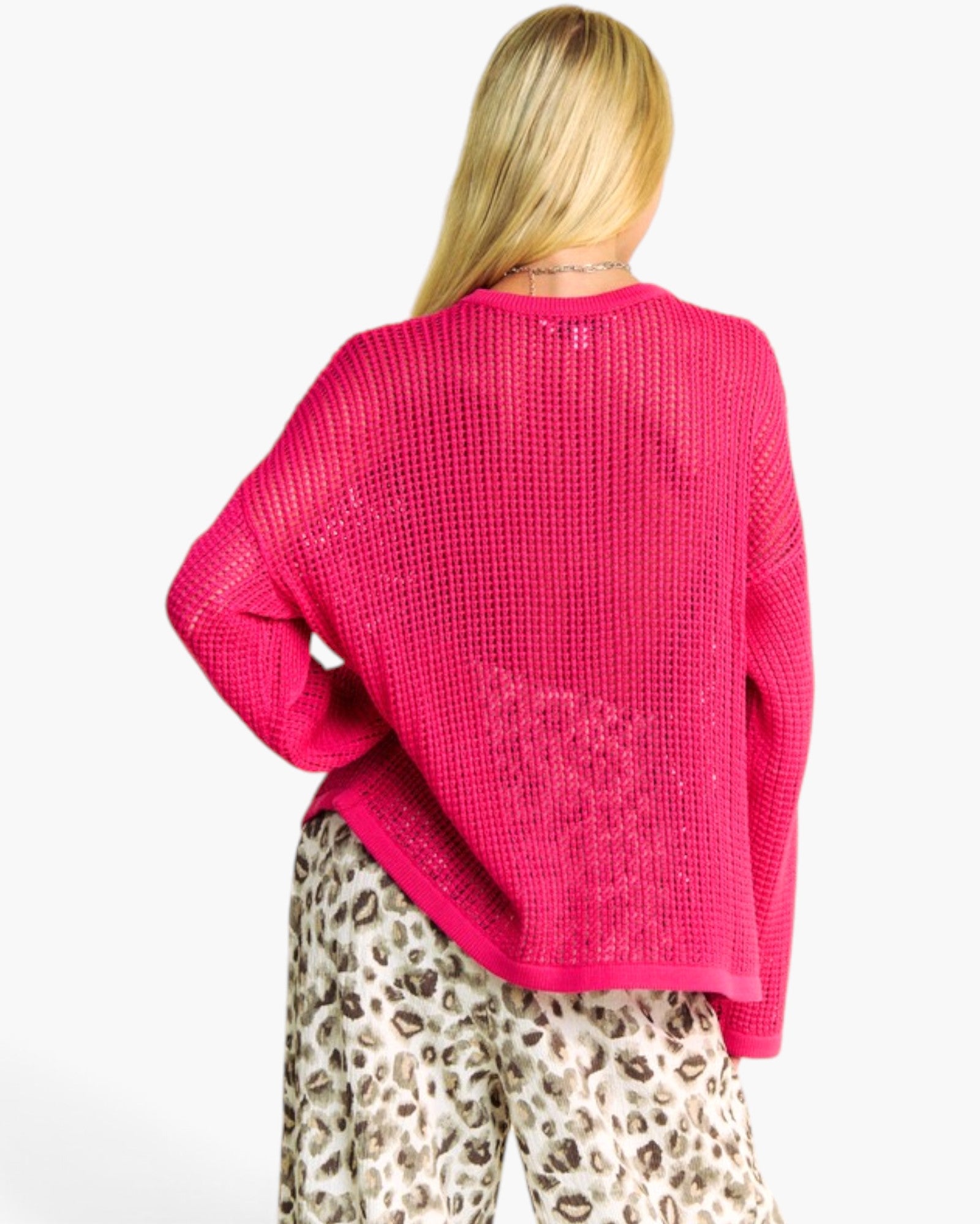 A woman shown from the back wearing a bright pink open-knit sweater and leopard-print pants against a plain white background.