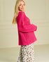 Woman wearing a bright pink knitted sweater and leopard print pants against a beige wall.