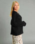 Woman wearing a black sweater and patterned pants against a gray background