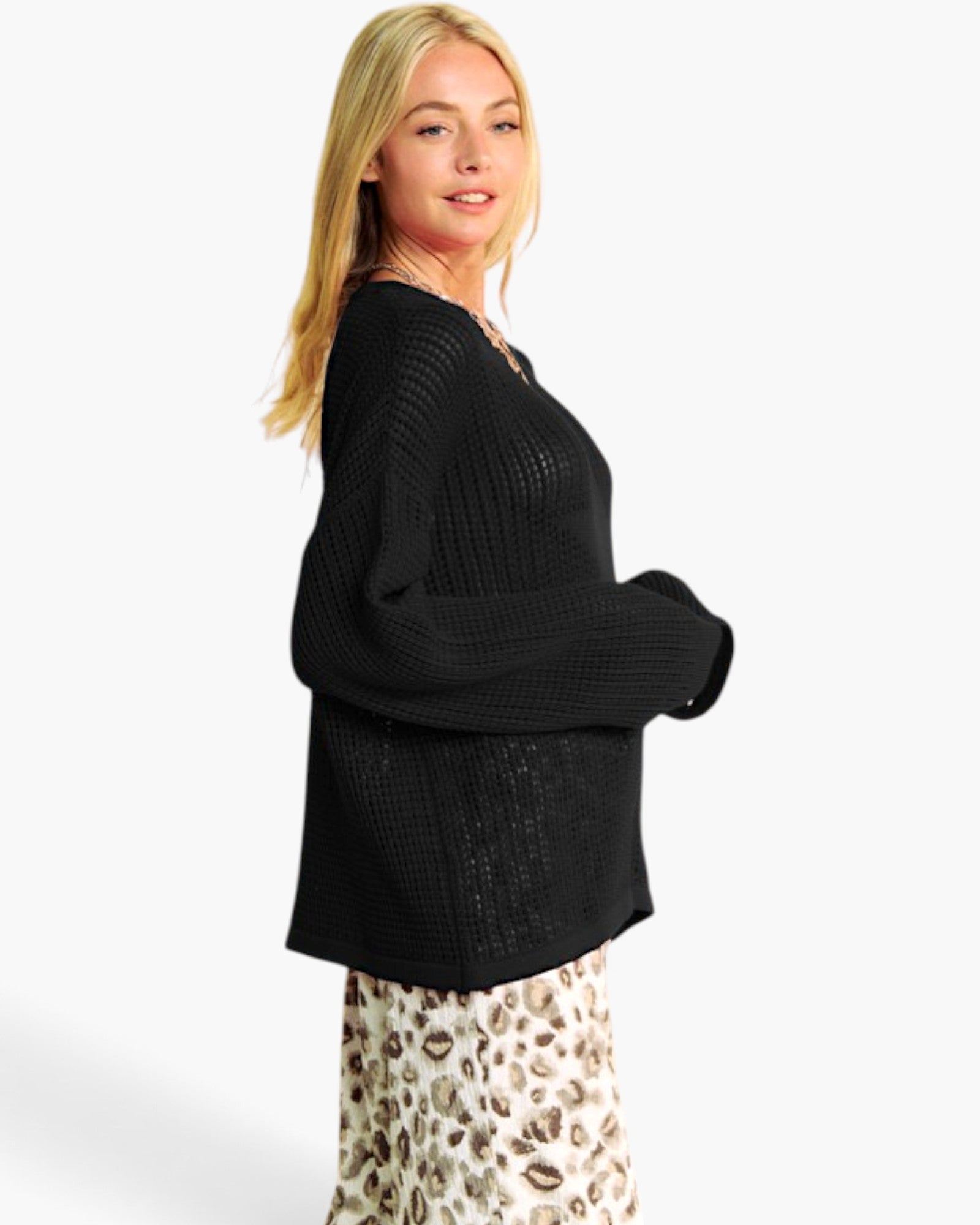 A woman modeling a black textured knit sweater with a wide collar and long sleeves, paired with a leopard-print skirt, against a plain white studio background.