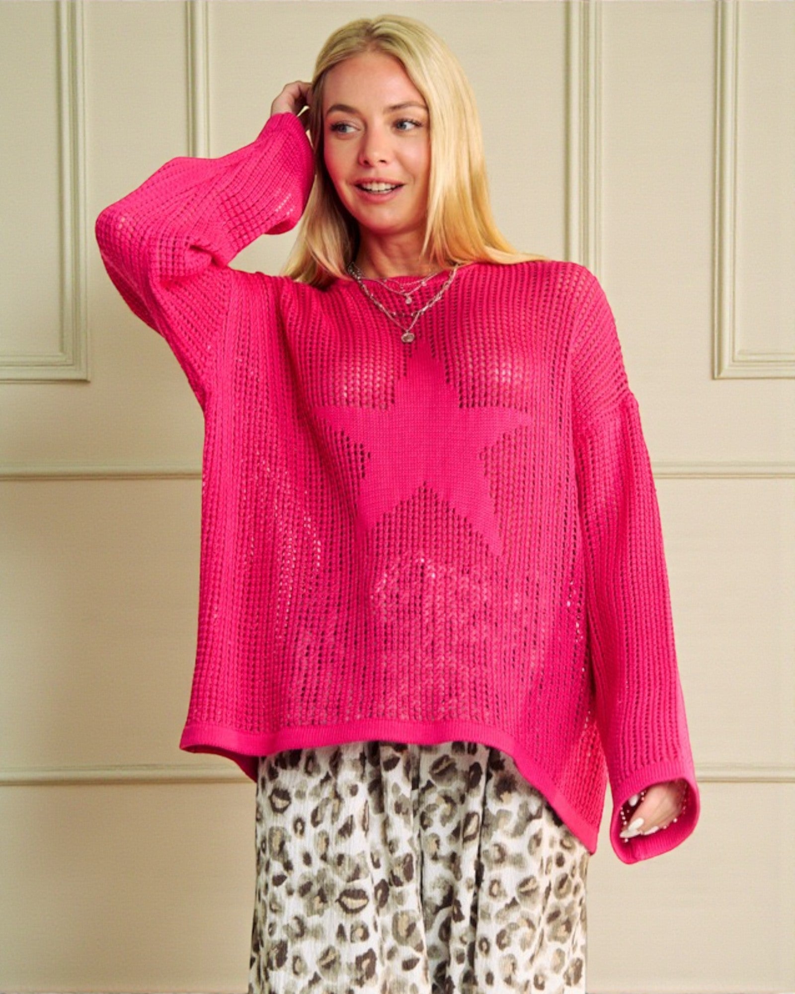 Woman wearing a bright pink sweater with a star pattern against a neutral wall.