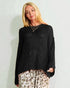 Woman wearing a black sweater and leopard print pants against a light background